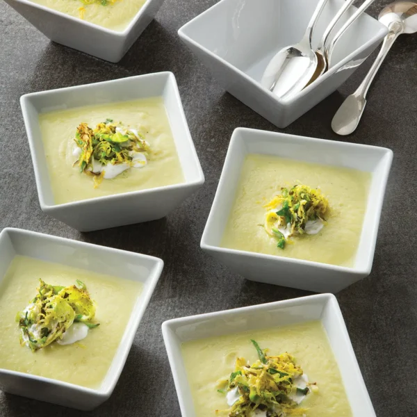 Multiple square bowls of Silky Cauliflower Curry Soup with Crispy Shaved Brussels Sprouts on a table.