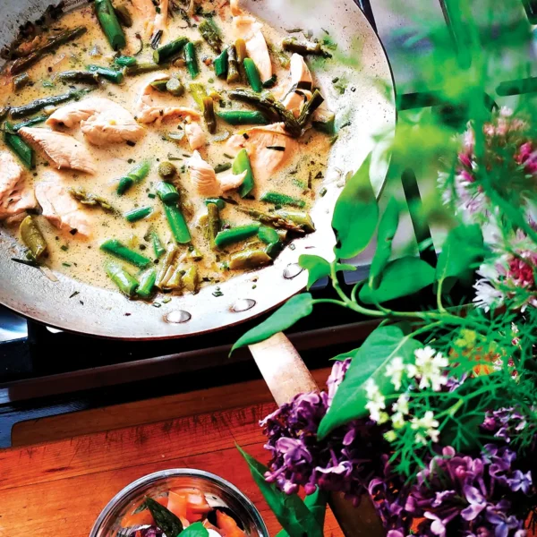 Frying pan containing asparagus with poached lemon tarragon chicken on the stove.