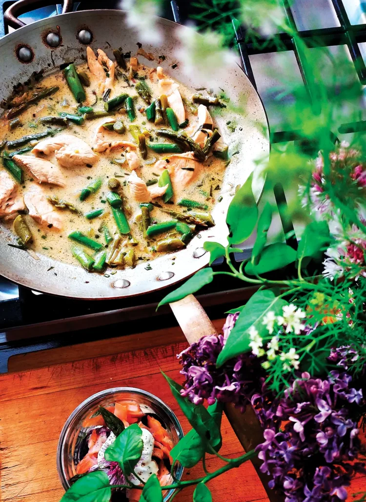 Frying pan containing asparagus with poached lemon tarragon chicken on the stove.