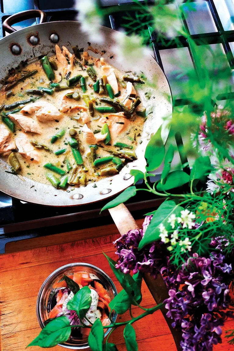 Frying pan containing asparagus with poached lemon tarragon chicken on the stove.