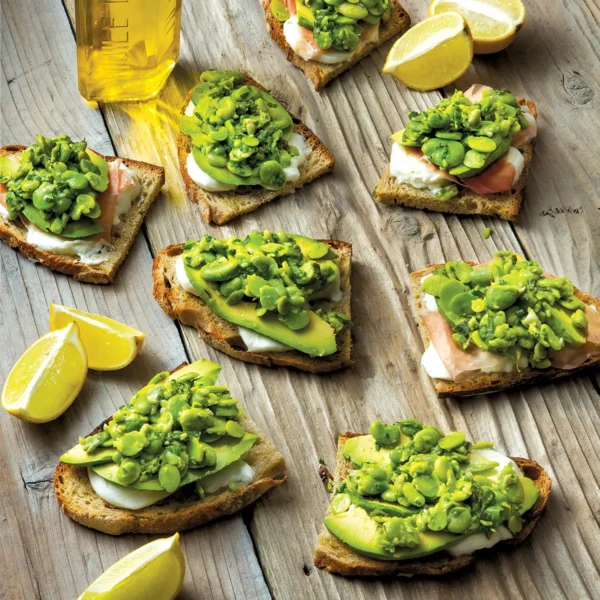 Several pieces of fava smash crostini with buffalo mozzarella arranged on a wooden table.