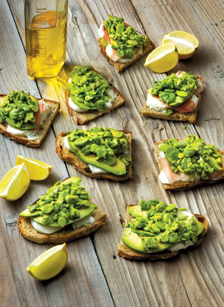 Several pieces of fava smash crostini with buffalo mozzarella arranged on a wooden table.