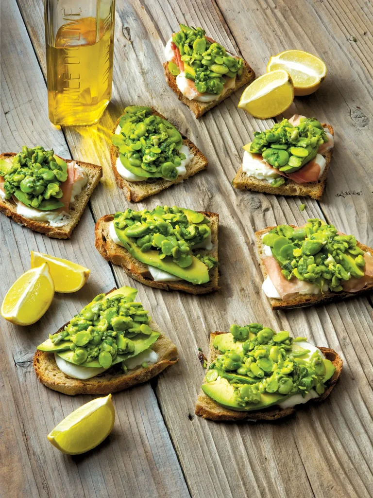 Several pieces of fava smash crostini with buffalo mozzarella arranged on a wooden table.