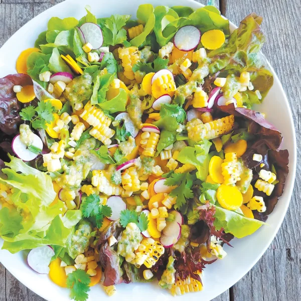 A large bowl containing grilled corn salad with pine nut pesto set on a wooden table