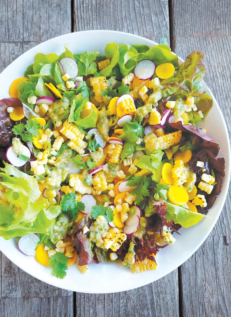 A large bowl containing grilled corn salad with pine nut pesto set on a wooden table