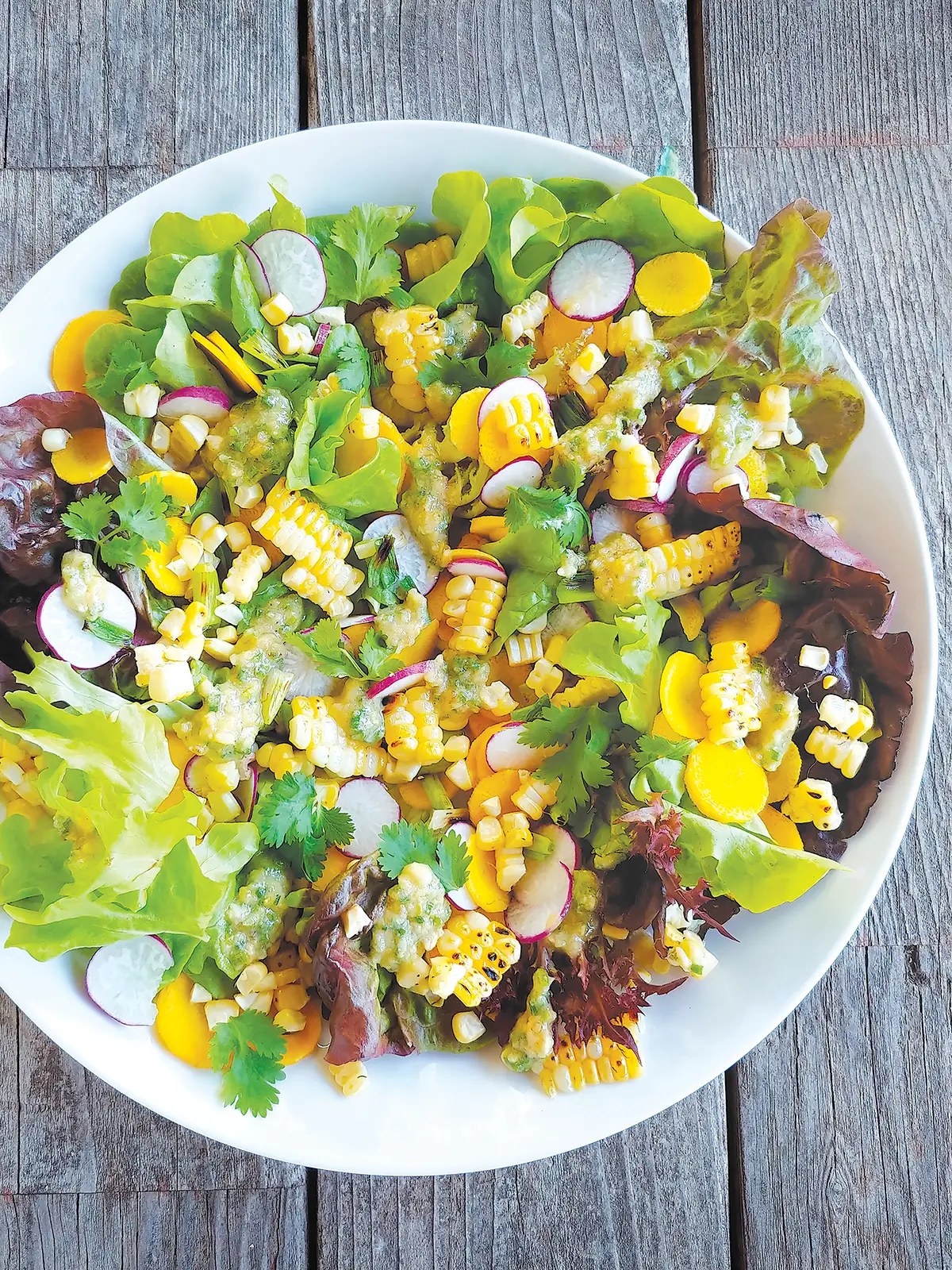 A large bowl containing grilled corn salad with pine nut pesto set on a wooden table