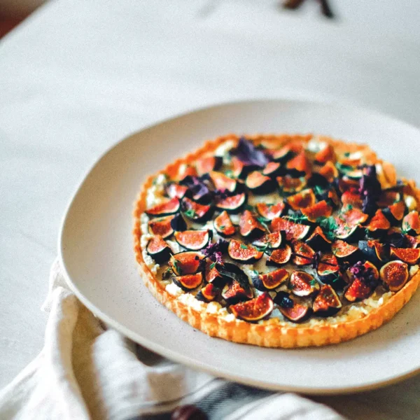 A plate with a Mission Fig and Whipped Feta Tart with Thyme and Spiced Honey set on a table.