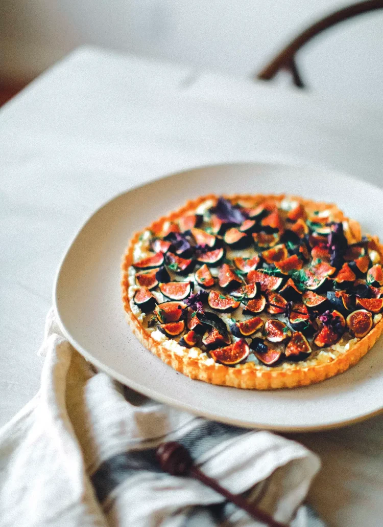 A plate with a Mission Fig and Whipped Feta Tart with Thyme and Spiced Honey set on a table.