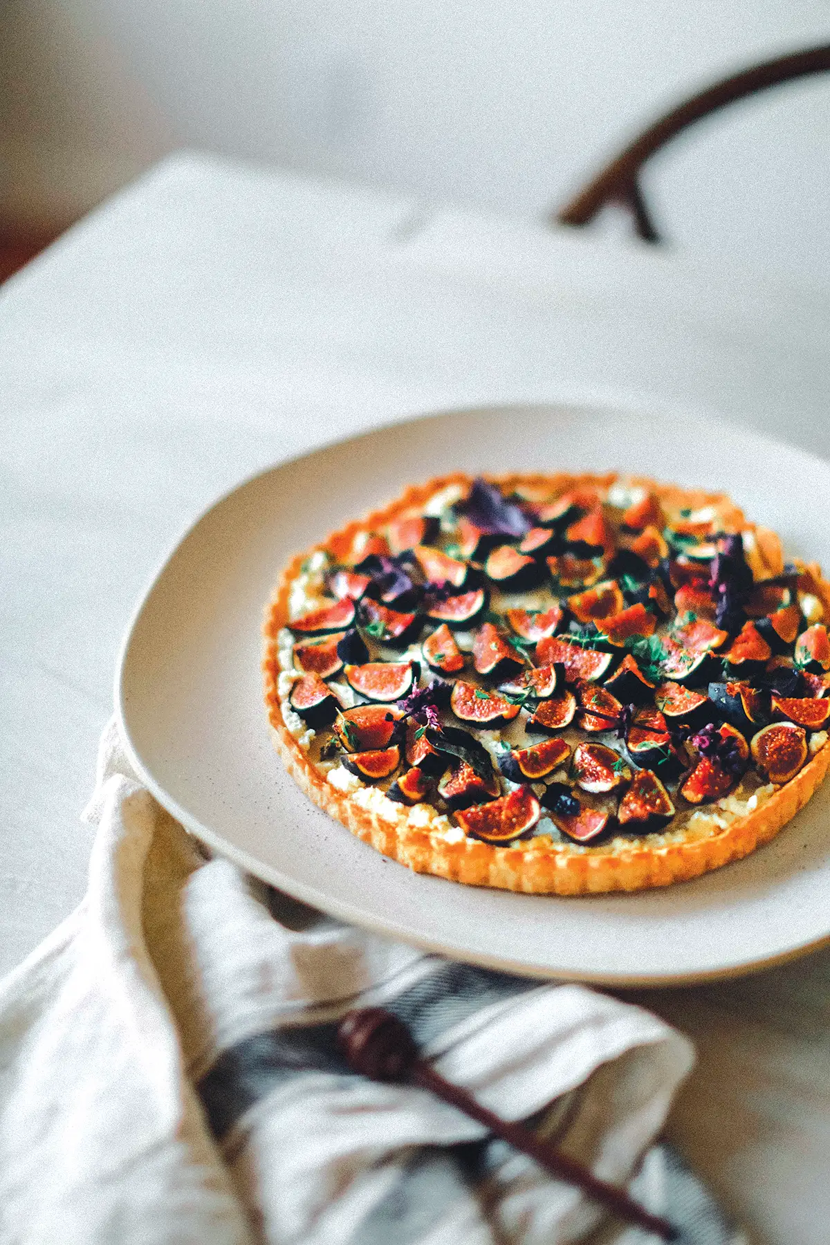 A plate with a Mission Fig and Whipped Feta Tart with Thyme and Spiced Honey set on a table.