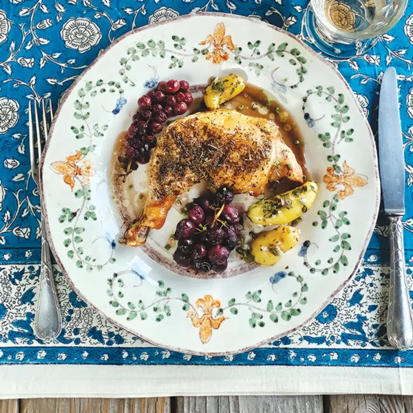 Provencal roasted chicken legs with champagne grapes plated and set on a blue table cloth.