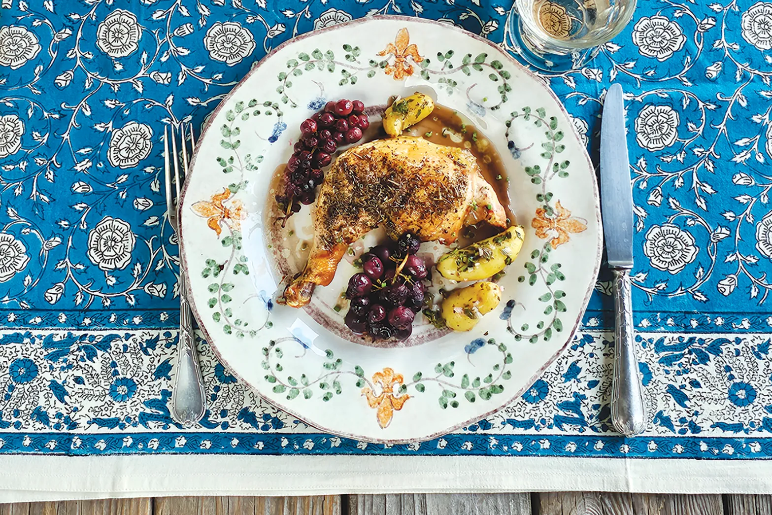 Provencal roasted chicken legs with champagne grapes plated and set on a blue table cloth.