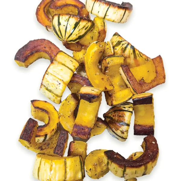 Pile of roasted delicata squash on a white background.