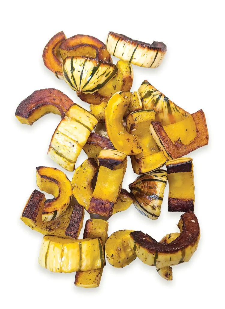 Pile of roasted delicata squash on a white background.