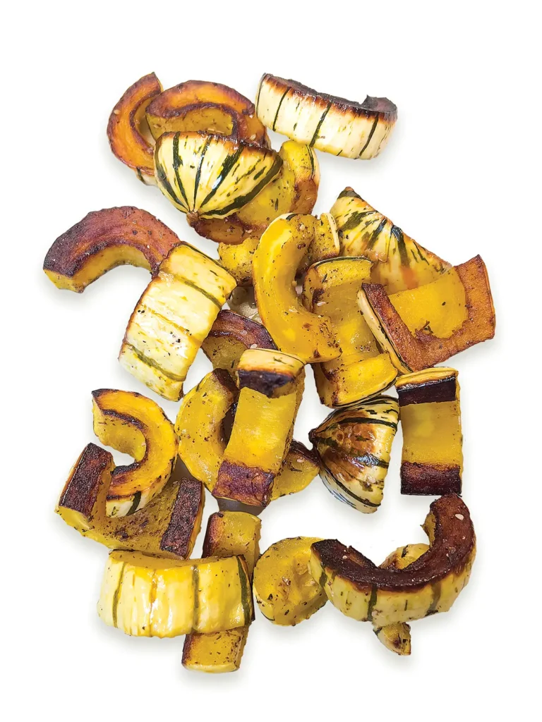 Pile of roasted delicata squash on a white background.