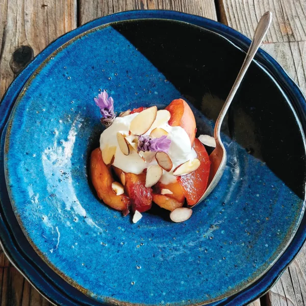 A blue bowl of Roasted White Peaches with Lavender and Crème Fraîche