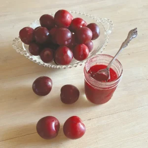 Plumbs in a bowl and on a table alongside a jar of spiced plum jam