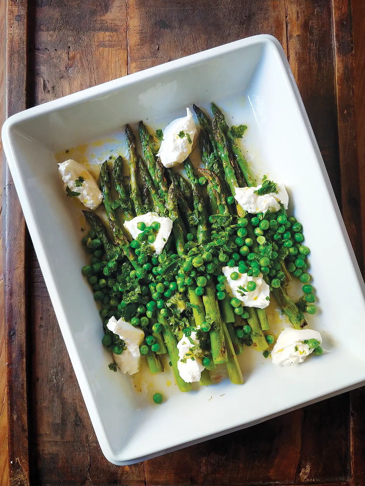 A white rectangular dish containing Grilled Asparagus with Spring Peas, Burrata and a Lemon-Mint Vinaigrette.