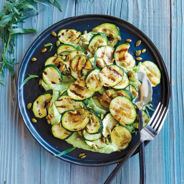 A plate of Grilled Zucchini with Avocado-Tarragon Crema on a wooden table top.