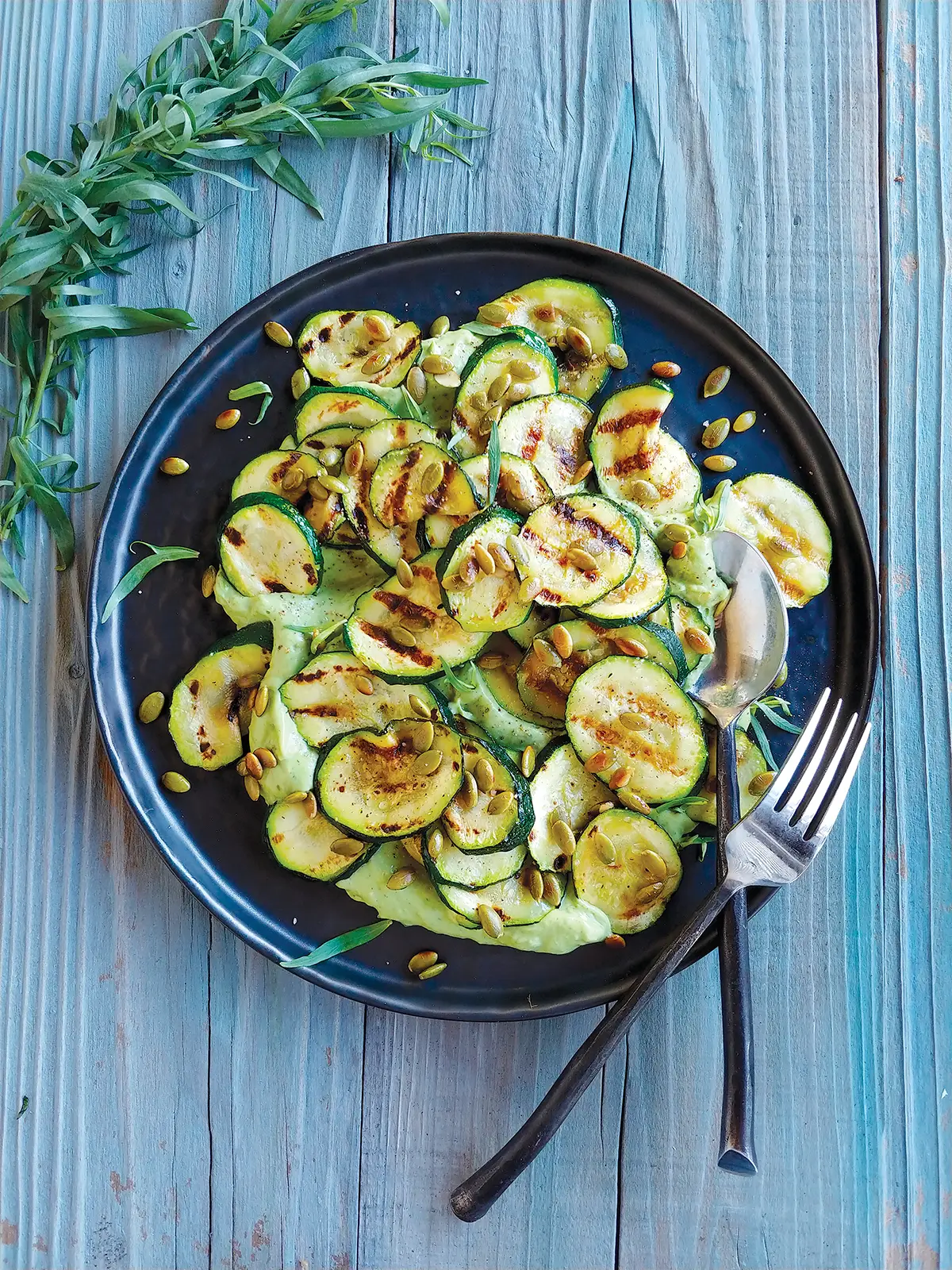 A plate of Grilled Zucchini with Avocado-Tarragon Crema on a wooden table top.