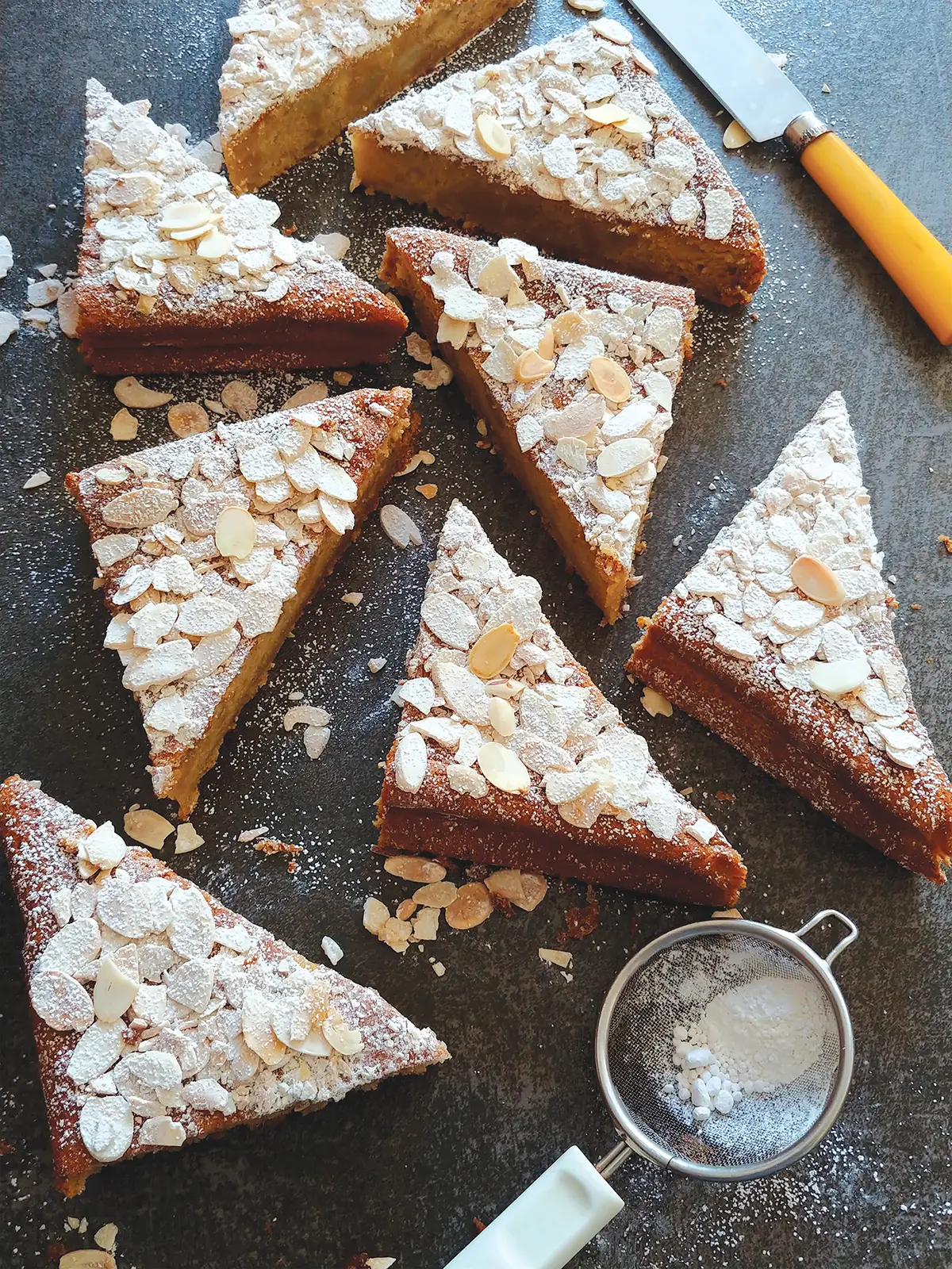 Triangular slices of pear almond cake arranged on a table and sprinkled with sliced almonds.