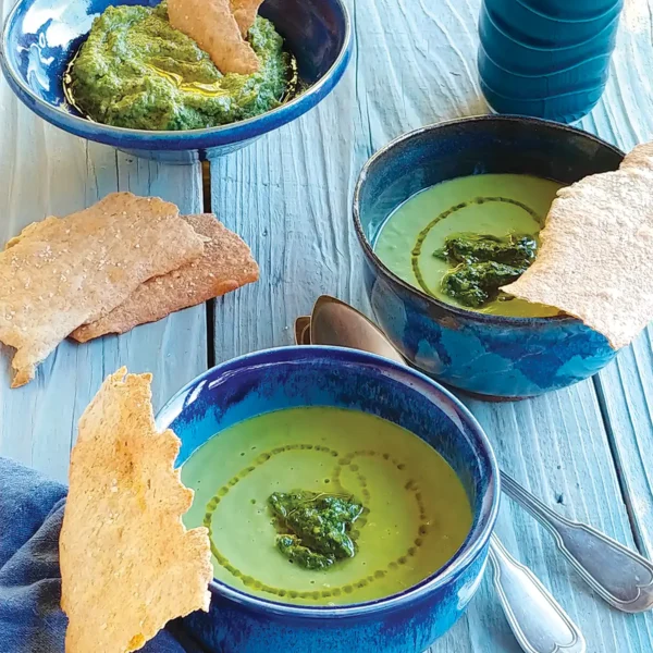 Bowls of Spring Pea and Leek Soup with Pesto on a wooden table top.