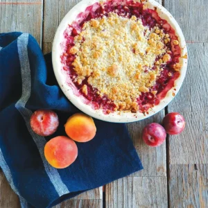 Stone Fruit Crumble in a round white bowl on a wooden table.