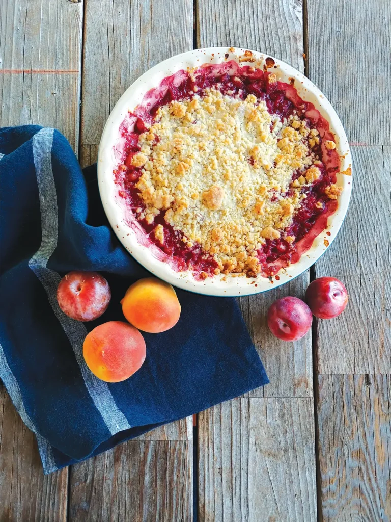 Stone Fruit Crumble in a round white bowl on a wooden table.