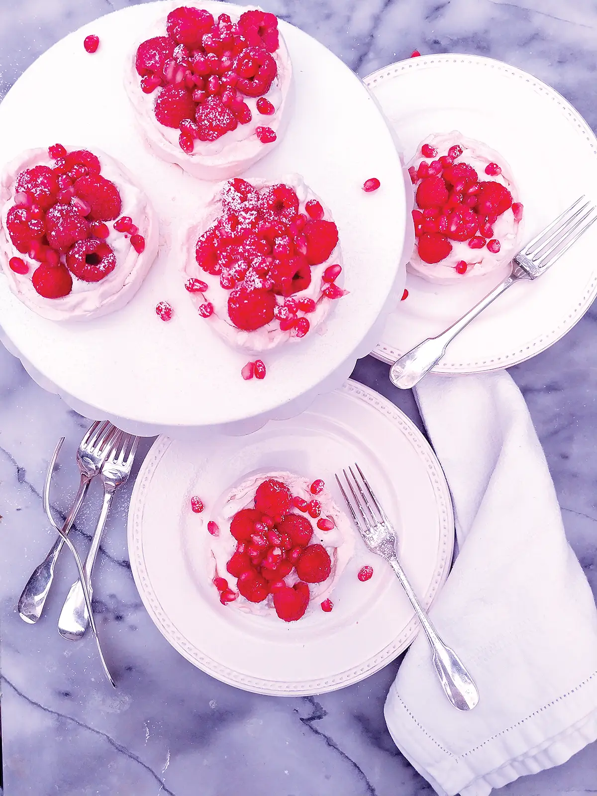 Plates of winter pavlova piled high with raspberries and pomegranate pips.