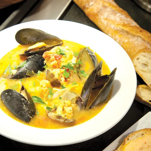 Bouillabaisse in a contrasting white bowl accompanied by baguette.