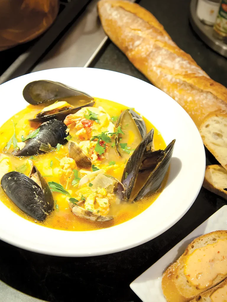 Bouillabaisse in a contrasting white bowl accompanied by baguette.