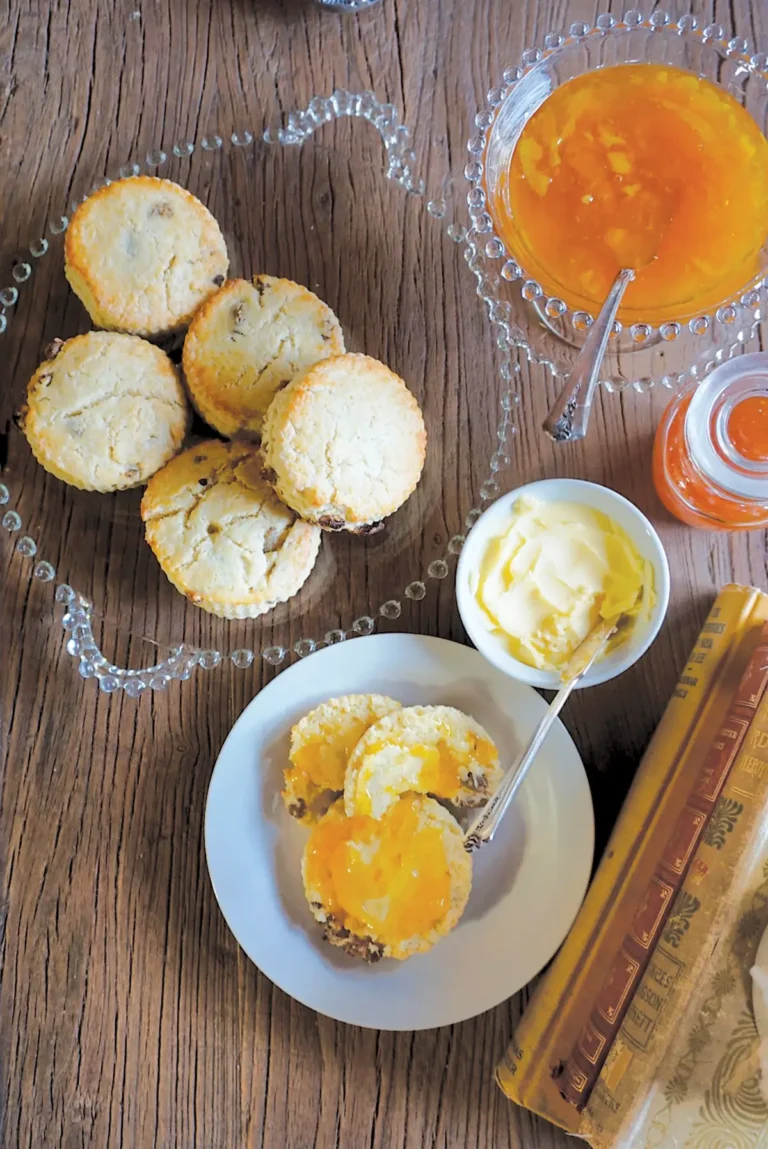 Table setting with Earl Grey tea-infused scones stacked on a glass serving dish, alongside sones on a plate with crème fraiche and apricot preserves.