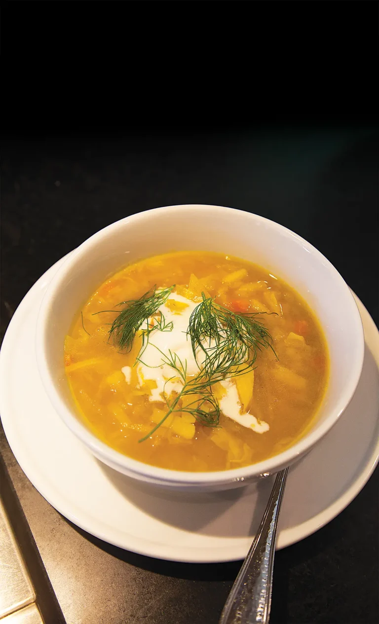 Bowl of golden beet borscht against a black background.