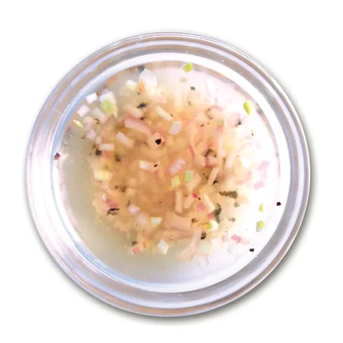 Small glass bowl of mignonette sauce set on a white background.