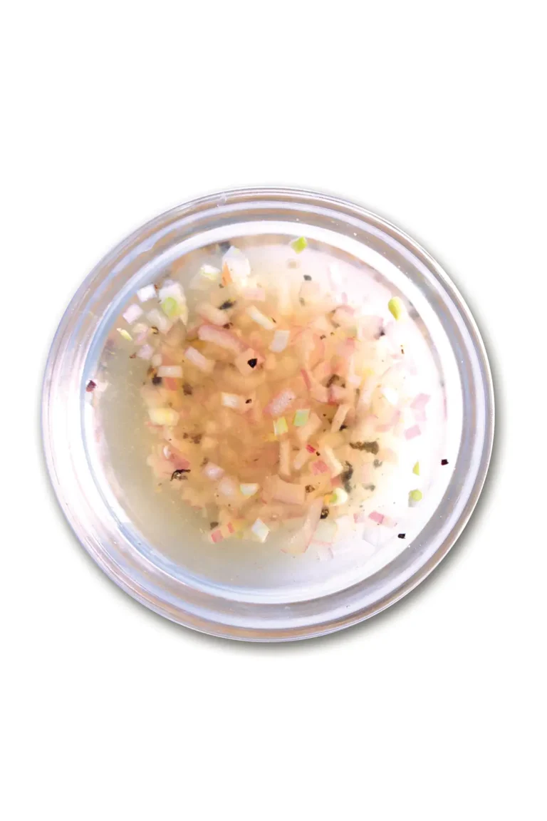 Small glass bowl of mignonette sauce set on a white background.