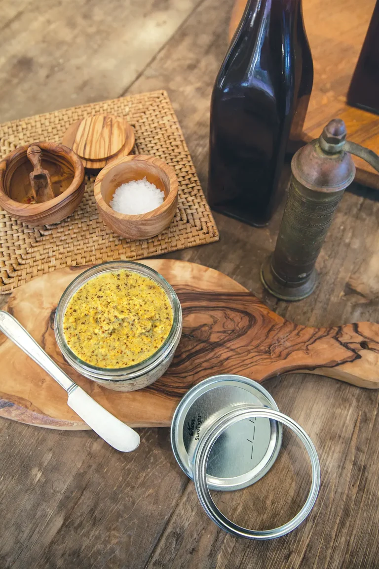 Small bowl of mustard set on a wooden cutting board.