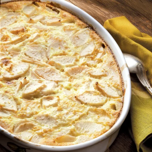 White oval dish containing Pear Clafoutis set on a wooden table.