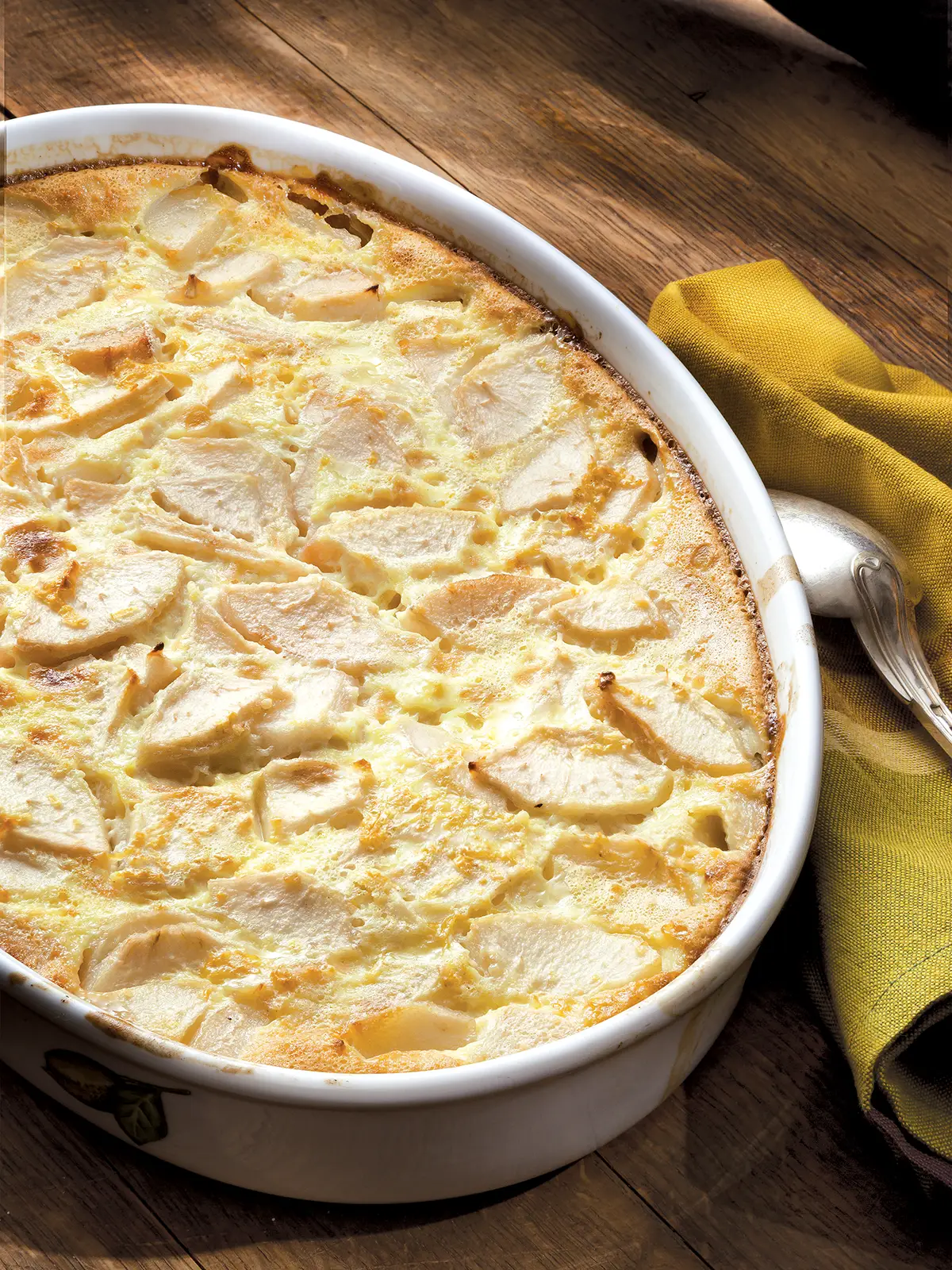 White oval dish containing Pear Clafoutis set on a wooden table.