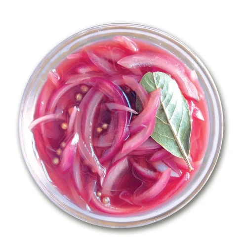 Small glass bowl holding pickled red onions set on a white background.