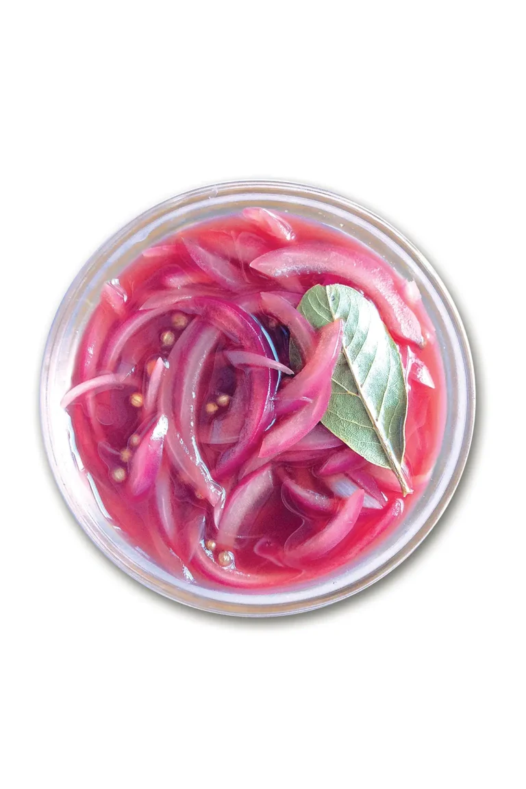 Small glass bowl holding pickled red onions set on a white background.