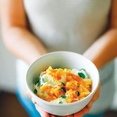 Woman holding a bowl of quick tumeric preserved citrus gremolata in open hands.