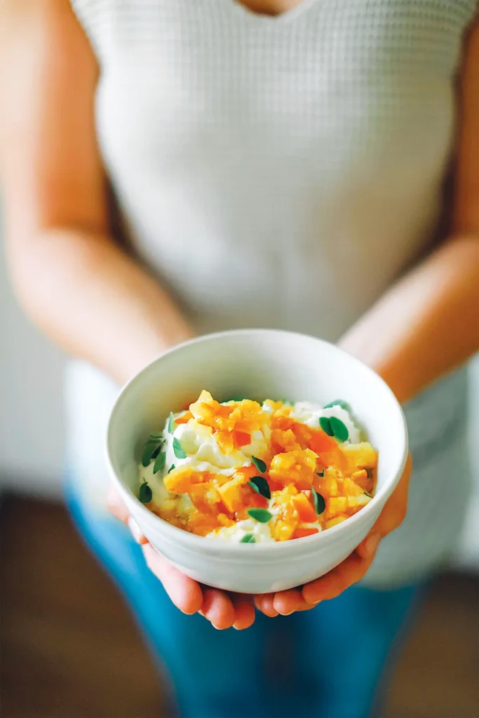 Woman holding a bowl of quick tumeric preserved citrus gremolata in open hands.