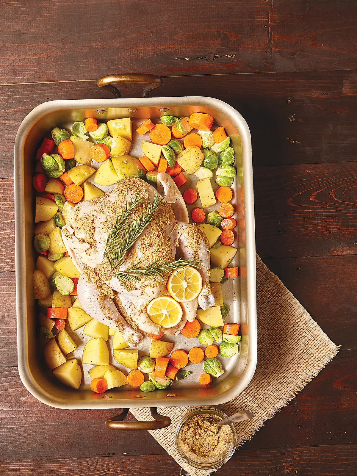 Roasting pan containing vegetables and a whole mustard coated chicken.