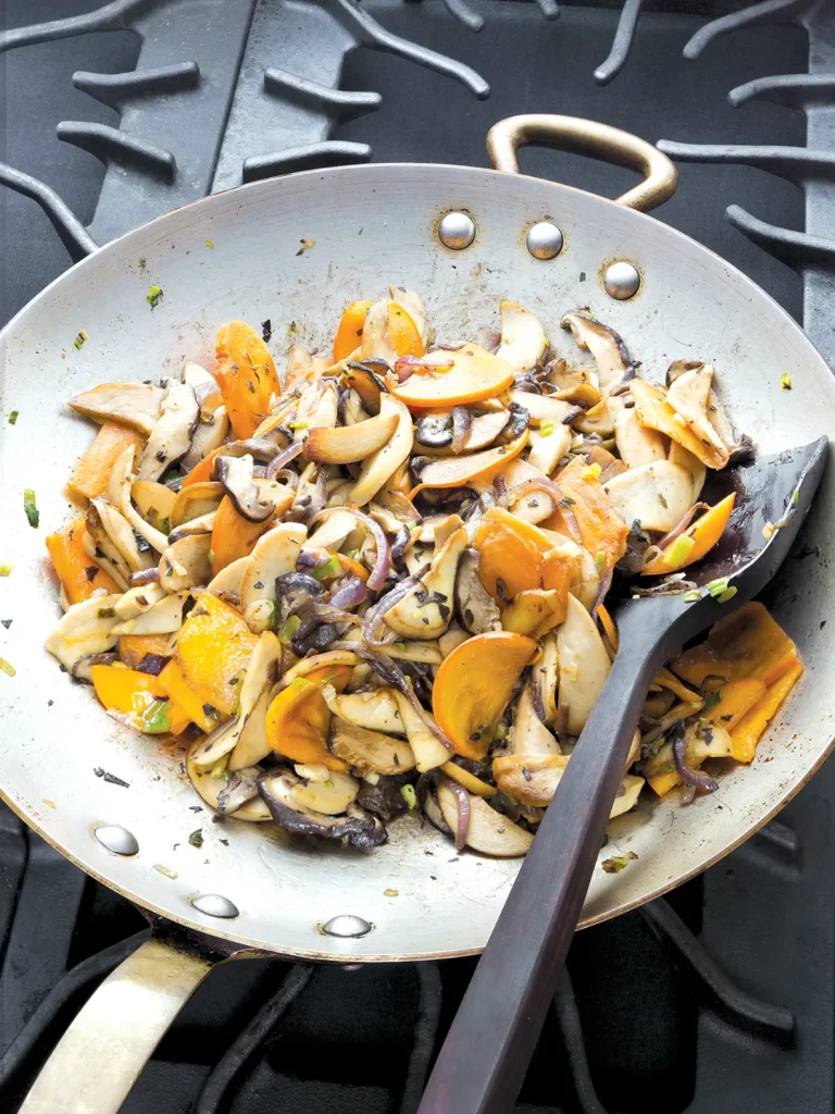 Wild mushroom and persimmon ragu in a wok on top of a stove.