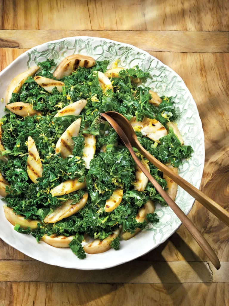 Grilled pear and roasted kale salad in an salad bowl with wooden spoons.