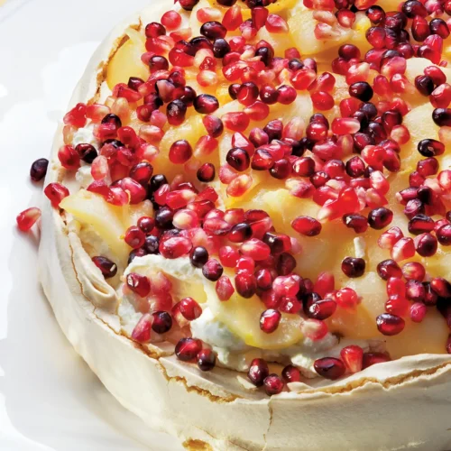 Pear and pomegranate pavlova on a white plate.