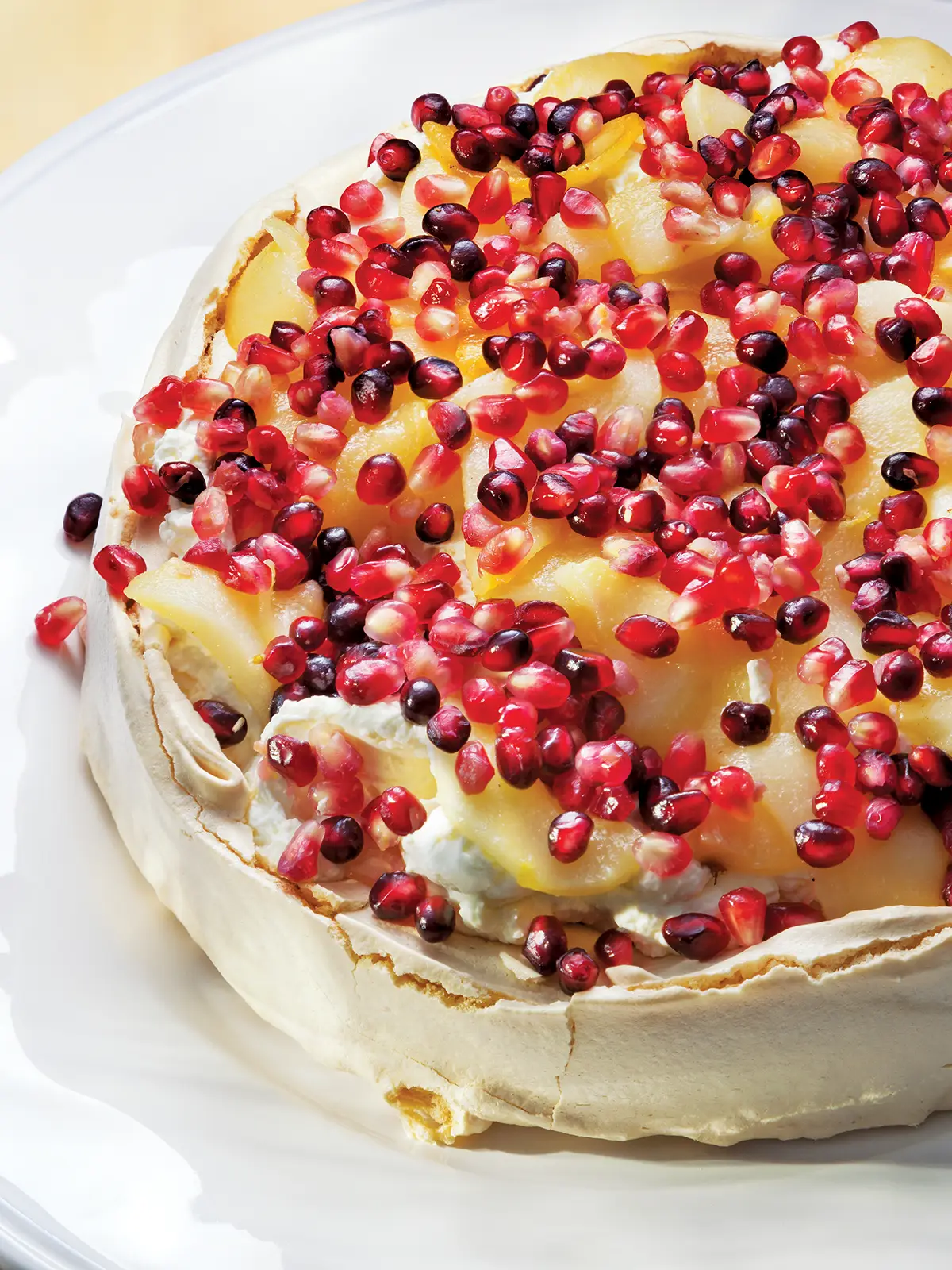 Pear and pomegranate pavlova on a white plate.