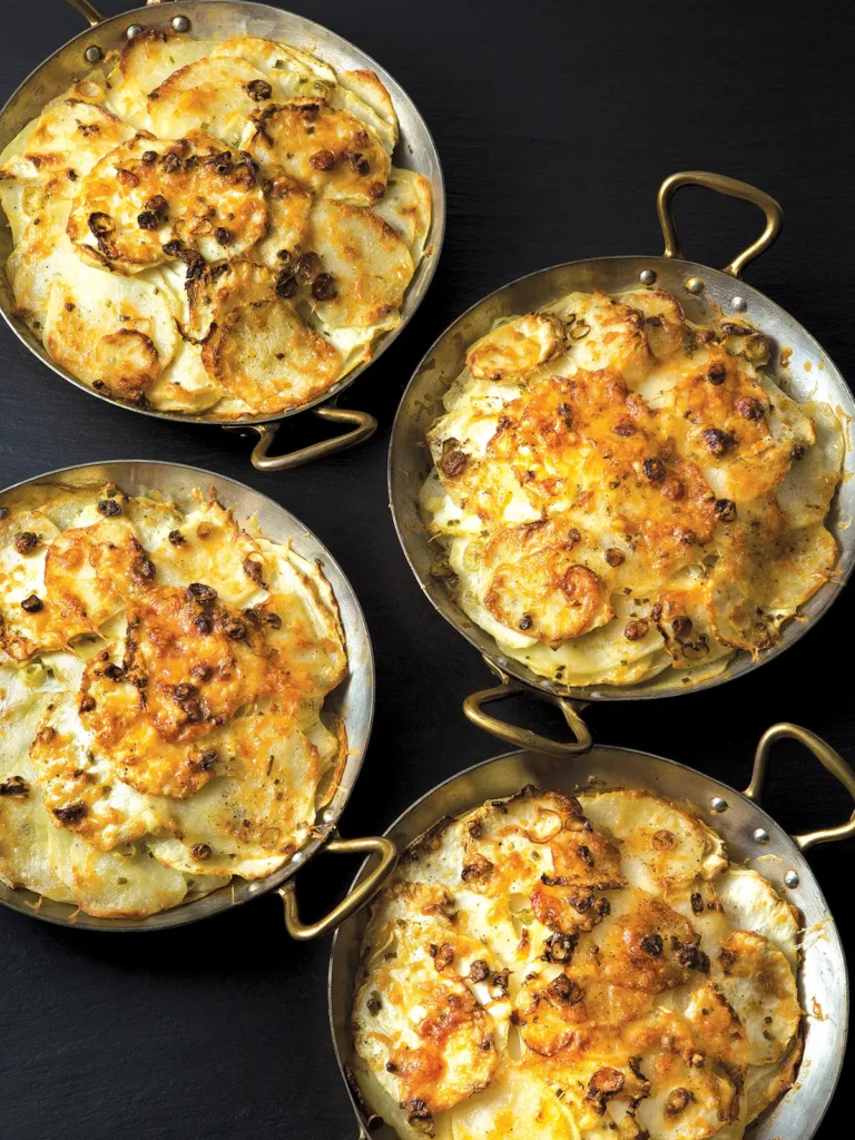 Four gratin pans with Potato and Celeriac Gratin arranged on a black background.