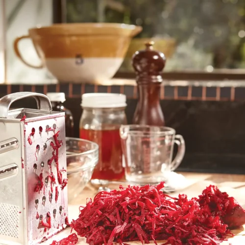 Countertop scene with a box grater and pile of grated red beets.