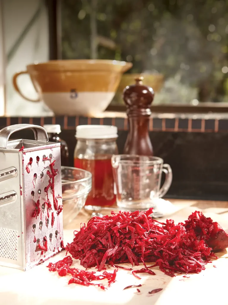 Countertop scene with a box grater and pile of grated red beets.