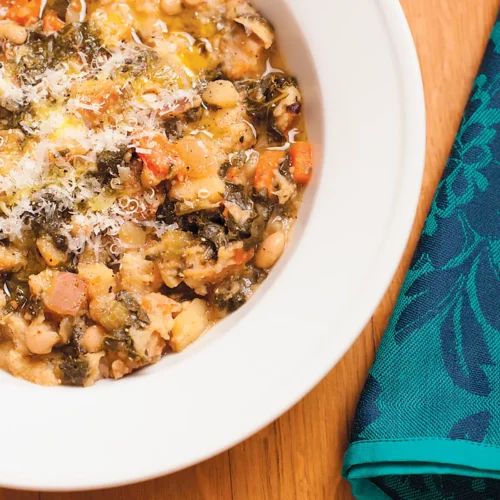 White bowl off Ribollita on wooden table with green napkin.